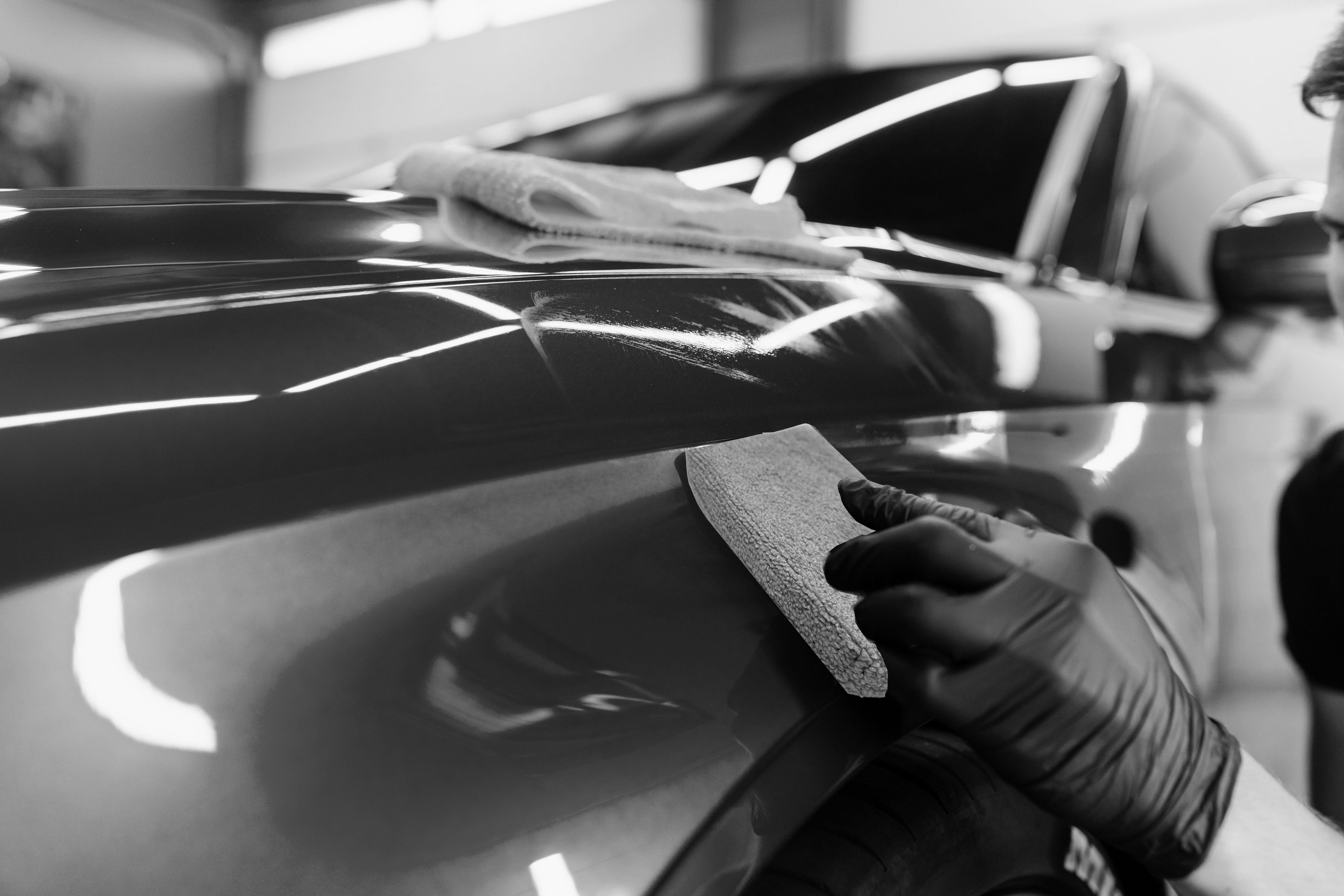 ceramic coating applied with a sponge applicator to a car fender with a microfiber towel folded on the hood 